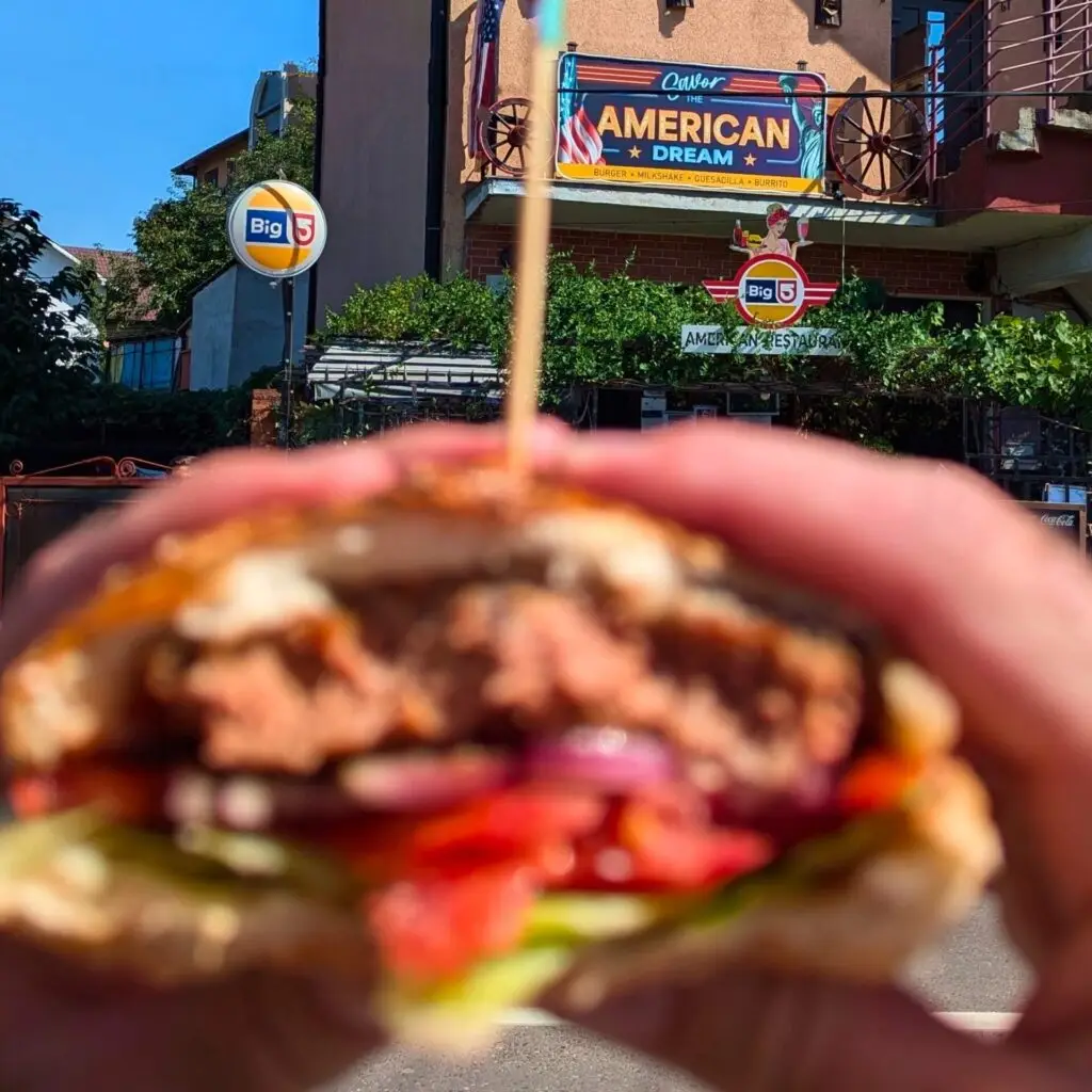 American Dream restaurant în fundal, burger în prim-plan.